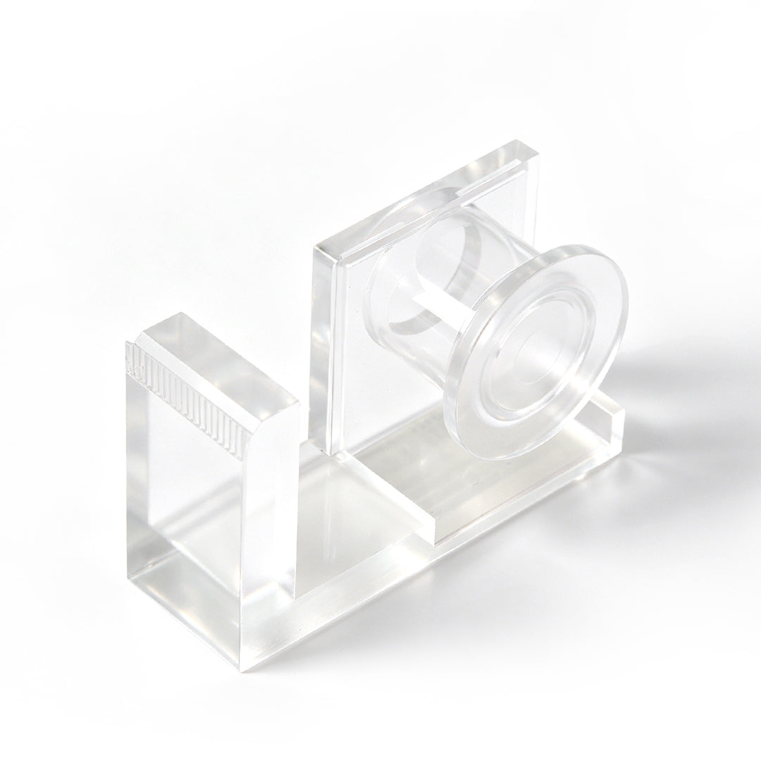 Clear acrylic lash tape dispenser with a pink tape roll and a built-in cutting edge, shown on a white background.