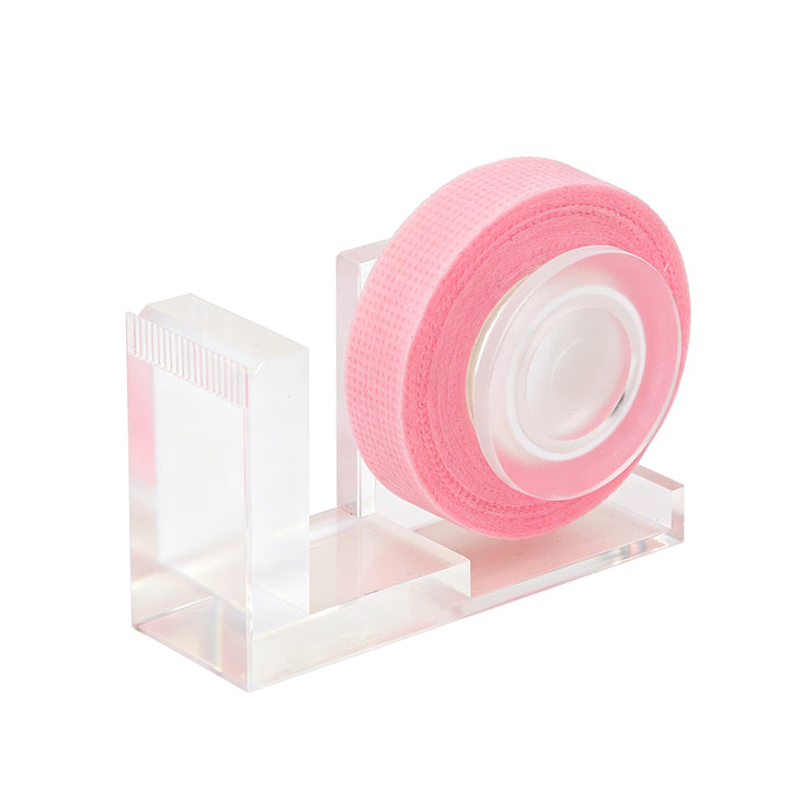 Clear acrylic lash tape dispenser with a pink tape roll and a built-in cutting edge, shown on a white background.